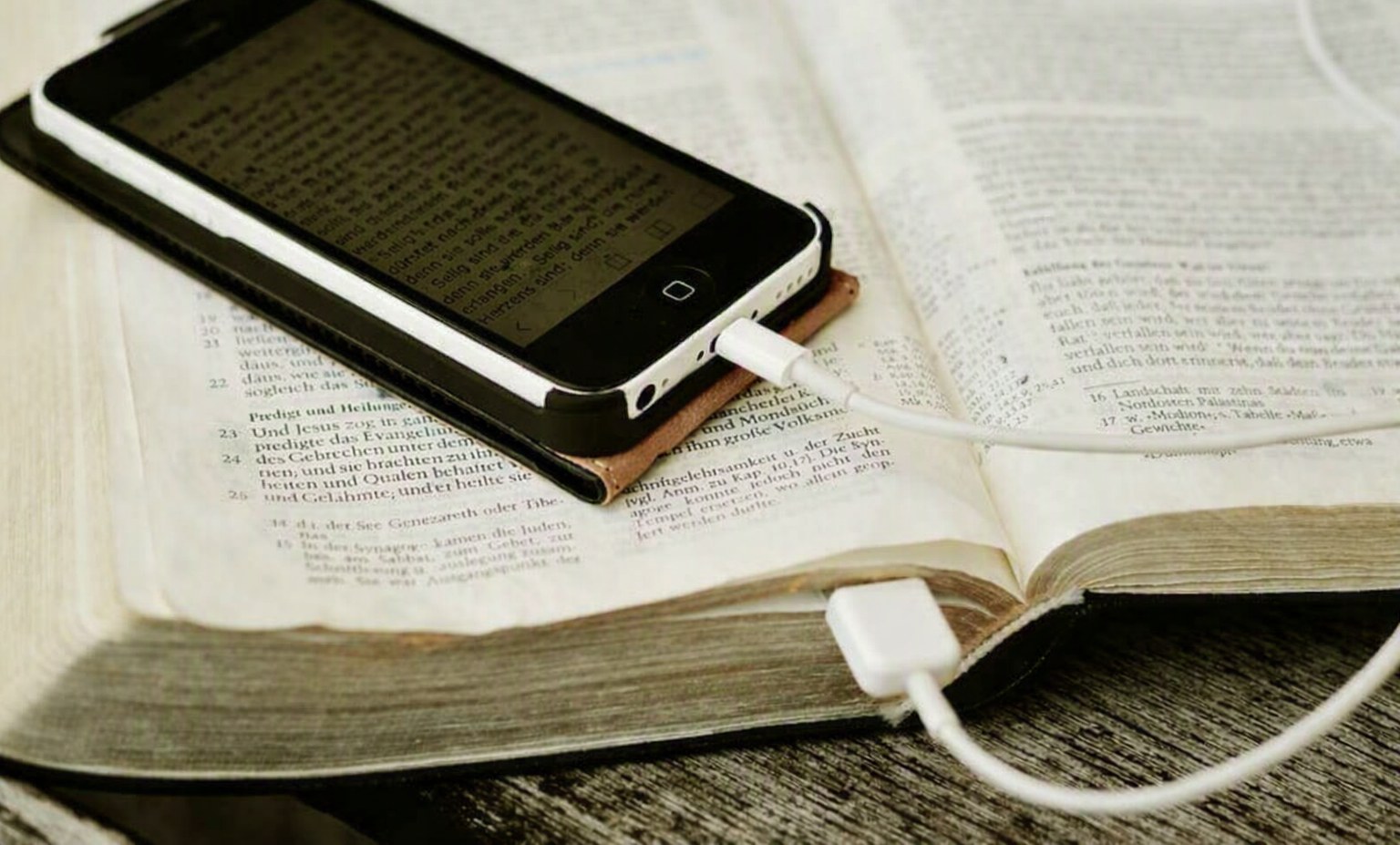 Smartphone met Bijbeltekst, opgeladen via USB, liggend op een opengeslagen Bijbel